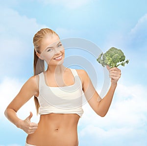 Woman pointing at her abs and holding broccoli