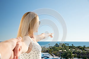 Woman is pointing with her finger to the sea from a balkony in summer holiday