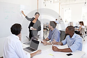 Woman pointing at whiteboard at a meeting in a busy office