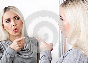 A woman points her finger at her reflection in the mirror.