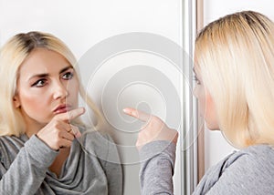 A woman points her finger at her reflection in the mirror.