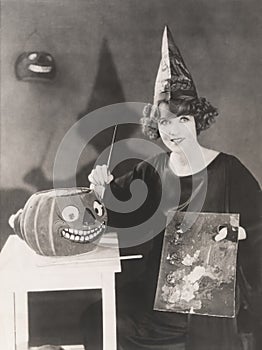 Woman in pointy hat painting a jack o'lantern