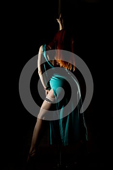 woman pole dancer in a long turquoise dress with a slit on a dark background