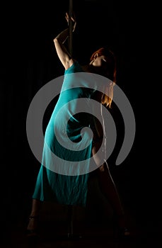 woman pole dancer in a long turquoise dress with a slit on a dark background