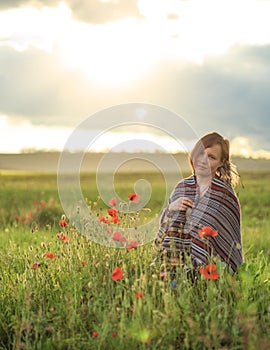 Woman in poncho sits on sunset flower field