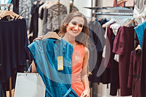 Woman pondering buying a blue dress in fashion store
