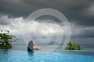 WOMAN IN POOL OVER OCEAN UNDER DARK STORM CLOUDS