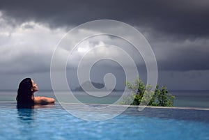 WOMAN IN POOL OVER OCEAN UNDER DARK STORM CLOUDS