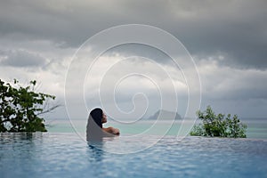 WOMAN IN POOL OVER OCEAN UNDER STORM CLOUDS