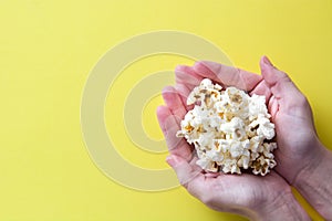 Woman with popcorn in hand on yellow background. Copyspace