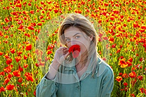 Woman on the poppies meadow. Beautiful girl on a poppy field outdoor. Poppies flowers near mouth.