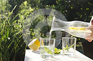 Woman poring water with lemon into glass.Refremnet time in the garden.Sunny and hot day in the garden