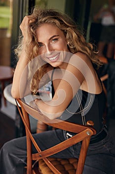 Woman Portrait. Beautiful Curly Blonde Model Resting On Chair In Cafe. Sexy Female Healthy Natural Look.