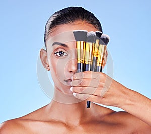 Woman, portrait and beauty, makeup brush on eye, foundation with cosmetics isolated on blue background, Indian model