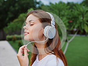 Woman portrait in headphones happiness smile with her eyes closed in a white T-shirt listening to music and walking down