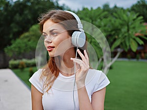 Woman portrait in headphones happiness smile in a white T-shirt listening to music and walking down the street, in front
