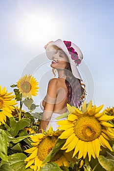 Woman poses in the agricultural field with sunflower on a sunny summer day