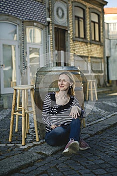 A woman poses sitting on the sidewalk at an outdoor cafe on the waterfront.