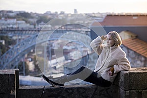 A woman poses on a stone wall in center of the Porto, Portugal.