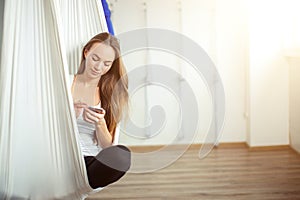 Woman posing in anti-gravity aerial yoga hammock. relax with phone