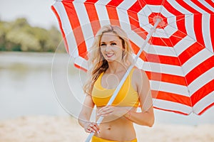 Woman posing with bir red and white stripped sun umbrella on the beach. S