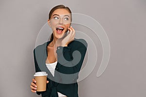 Woman posing isolated over grey wall background drinking coffee talking by mobile phone.