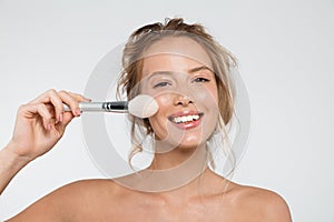 Woman posing isolated over white wall background holding makeup brushes