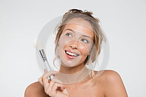 Woman posing isolated over white wall background holding makeup brushes