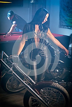 Woman posing near motorbikes, man playing billiards