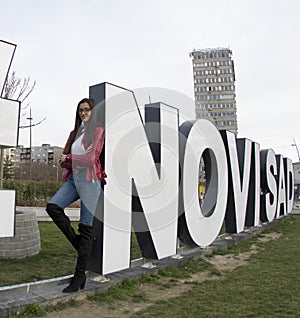 Woman is posing next to the capital letters where Novi Sad is written.
