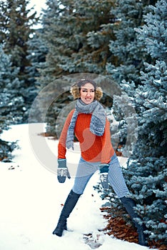 Woman is posing in winter forest, beautiful landscape with snowy fir trees. Dressed in red sweater and earmuffs
