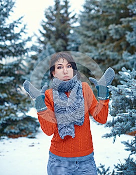 Woman is posing in winter forest and and puffs out her cheeks, beautiful landscape with snowy fir trees. Dressed in red sweater