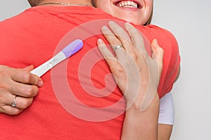Woman with positive pregnancy test hugging her husband