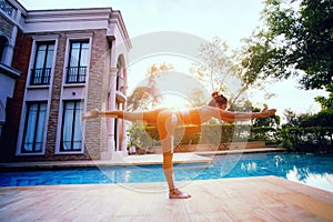 Woman posting warrior yoga pose beside sport water pool