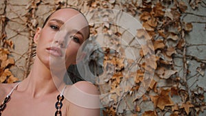 Woman posturing autumn leaves on wall close up. Sensual model looking camera