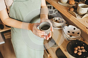 Woman potter in apron holds products in her hands.