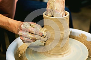 The woman potter& x27;s hands formed by a clay pot on a potter& x27;s wheel. The potter works in a workshop