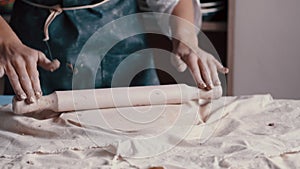 A woman potter wearing an apron preparing and rolling clay