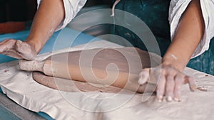 A woman potter wearing an apron preparing and rolling clay