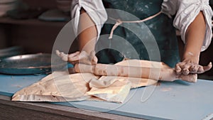 A woman potter wearing an apron preparing and rolling clay with a rollingpin