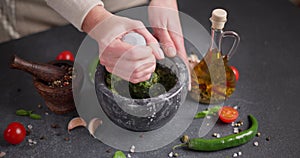 woman pounding in a stone marble mortar green sauce chopped ingredients - capers, fennel and basil