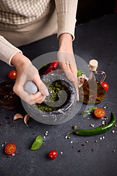 woman pounding in a stone marble mortar green sauce chopped ingredients - capers, fennel and basil