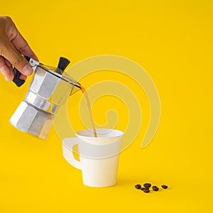 Woman poured Moka coffee into the white cup with roasted, coffee beans on a yellow paper background. Copy space for your text