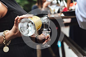 Woman pouring alcohol into glass. Closeup of female hands pouring transparent alcoholic drink from bottle. Celebration