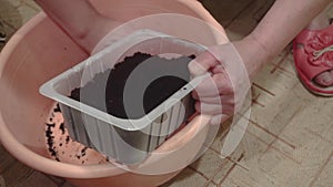 Woman pouring black soil into a pot for planting seeds