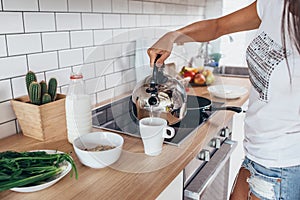 Woman pouring boiling water into a cup from kettle.