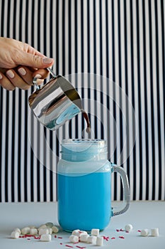 Woman is pouring coffee in stylized mason jar cup of colored blue milk on a black-and-white background. Milk shake, cocktaill, fra