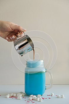 Woman is pouring coffee in stylized mason jar cup of colored blue milk. Milk shake, cocktaill, frappuccino.
