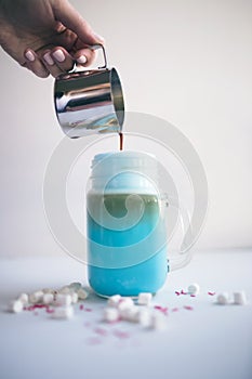 Woman is pouring coffee in stylized mason jar cup of colored blue milk. Milk shake, cocktaill, frappuccino. Unicorn coffee