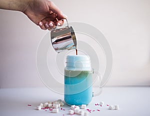 Woman is pouring coffee in stylized mason jar cup of colored blue milk. Milk shake, cocktaill, frappuccino. Unicorn coffee